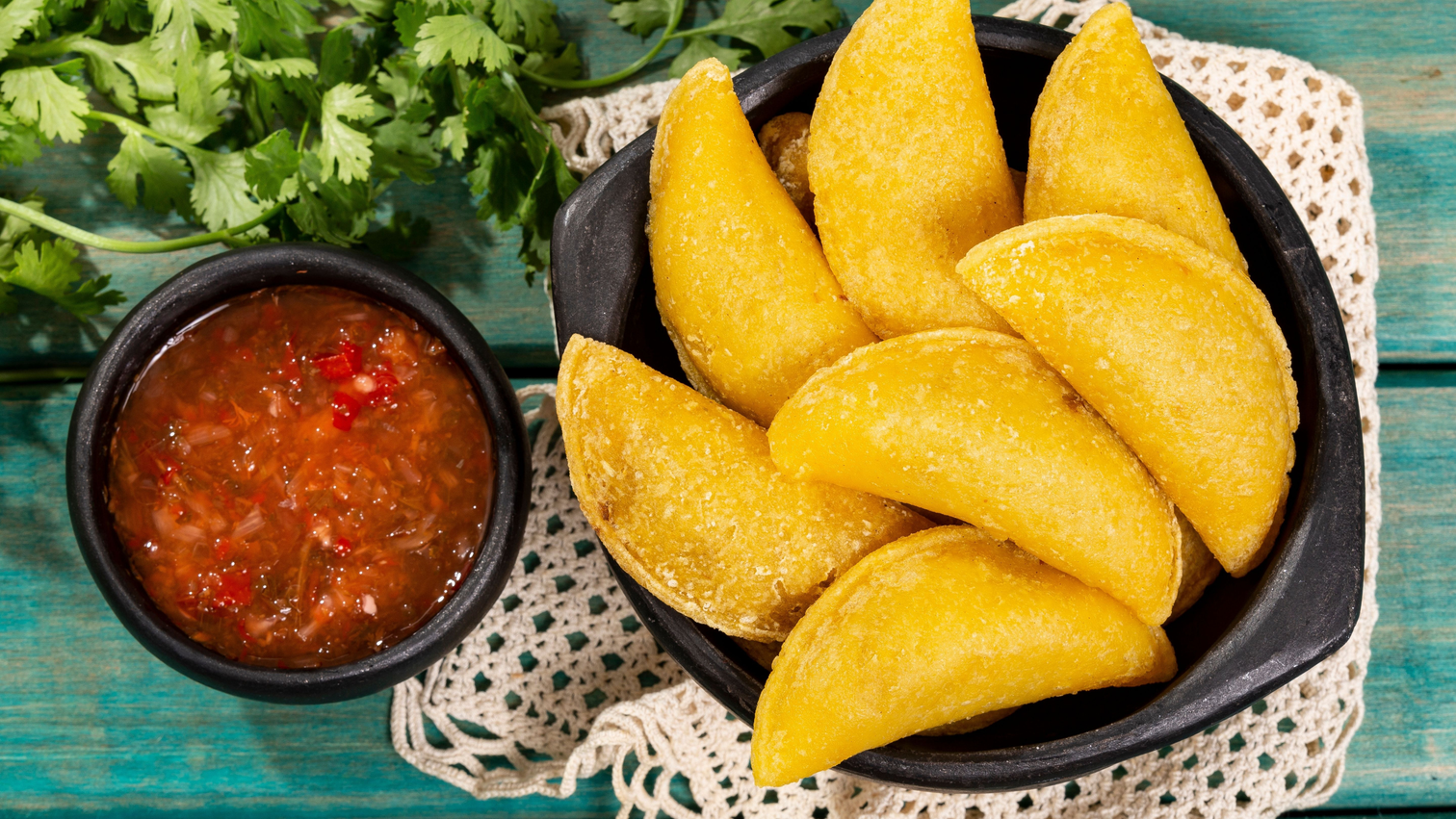 7 crunchy colombian empanadas in a bowl with red sauce on the side