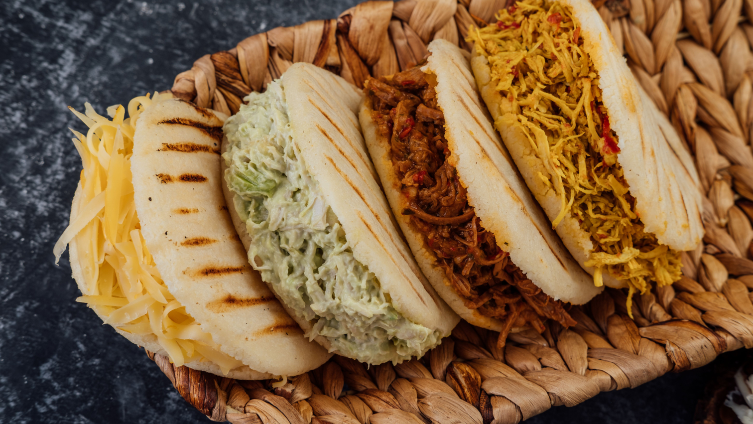 4 Venezuelan Arepas filled with shredded yellow cheese, reina pepeada (avocado, mayo and shredded chicken), shredded beef and shredded chicken all placed in a bascket