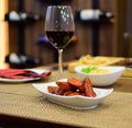 Fried copped chistorras served in a white bowl with a red wine glass on a wooden table with yute table mats